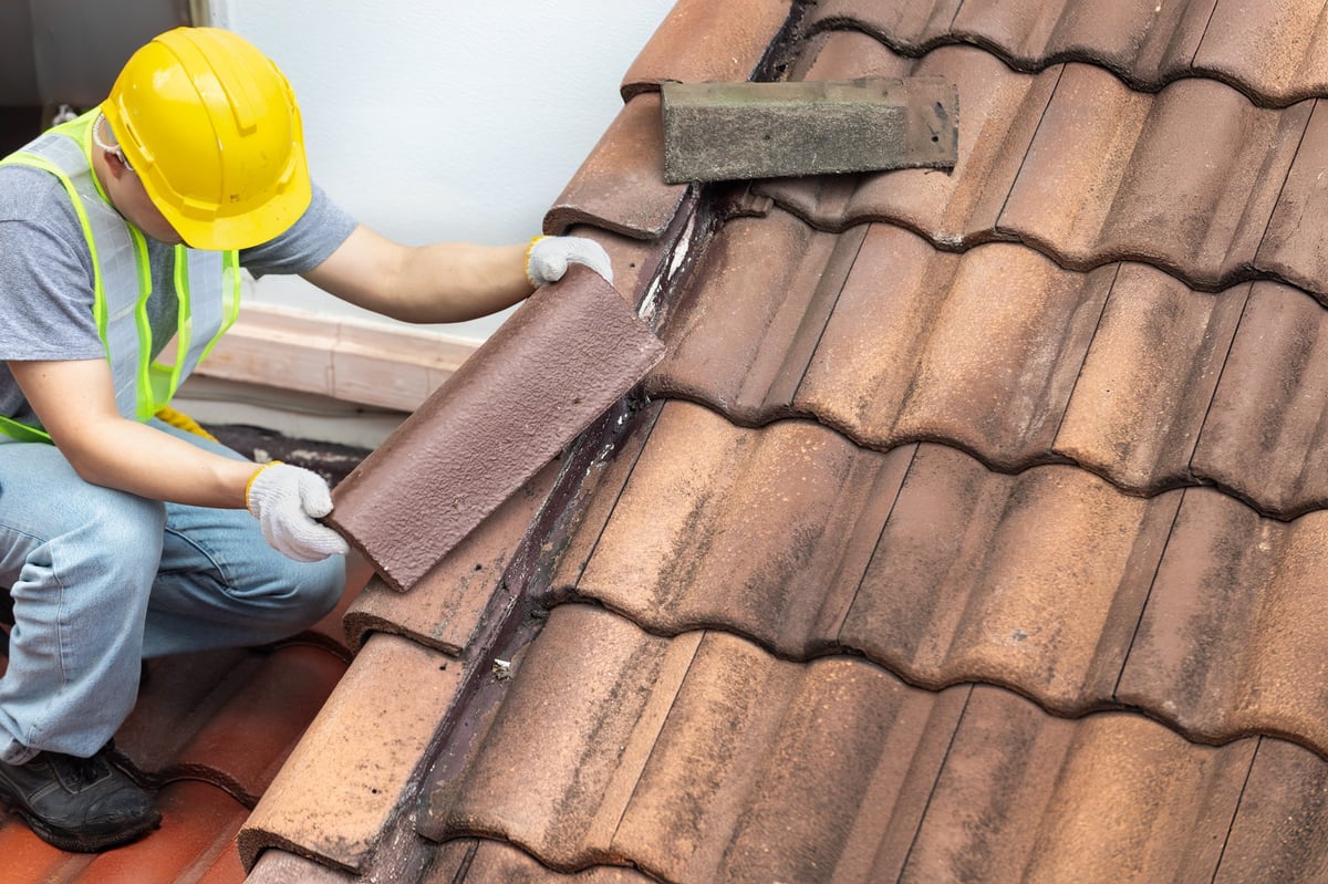 Worker fixing eaves and tiles of the old roof