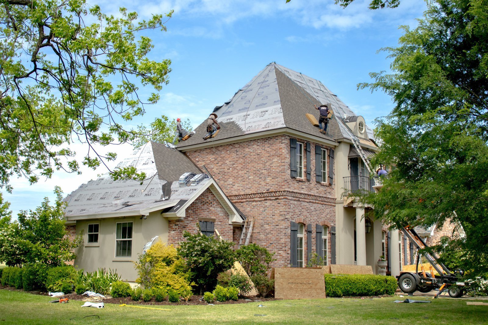 Victorian brick mansion with mansard roof and white trim surrounded by green lawn and mature trees