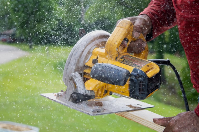 Person using a yellow circular saw with water spray on wood outdoors