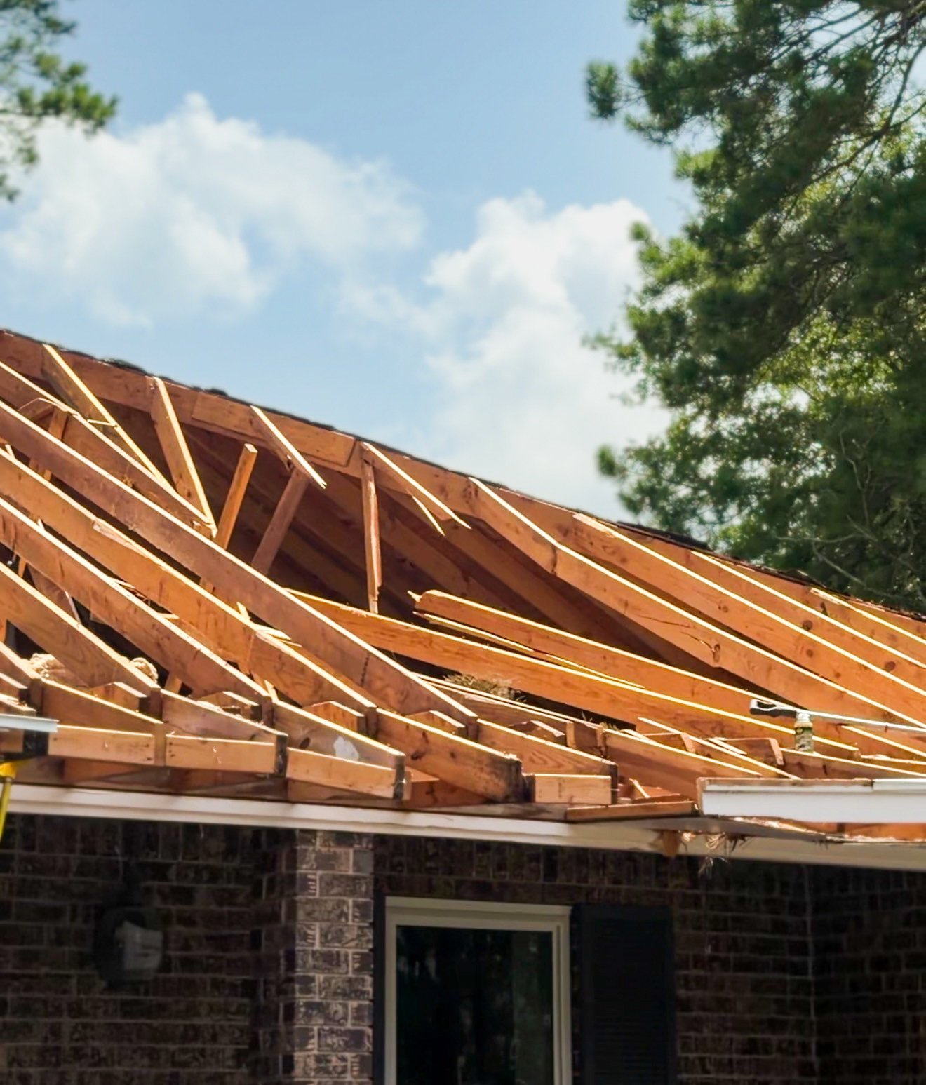 Roof under construction with exposed wooden rafters and trusses on a brick house, clear sky visible above