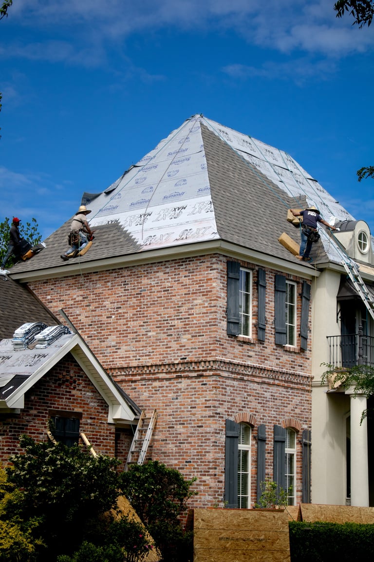 Roofers installing shingles on a brick house with mansard roof during construction in sunny weather